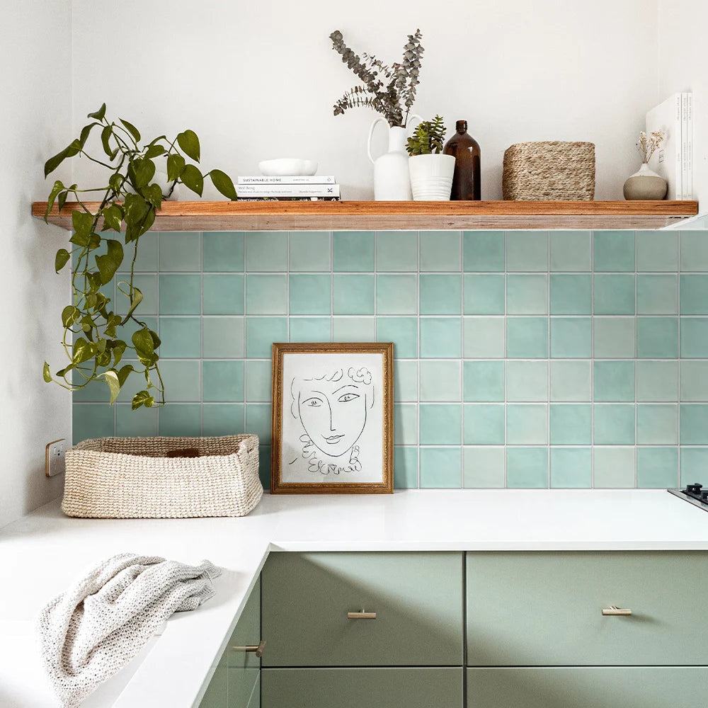 Kitchen with green tiled backsplash, white countertop, and wooden shelf.