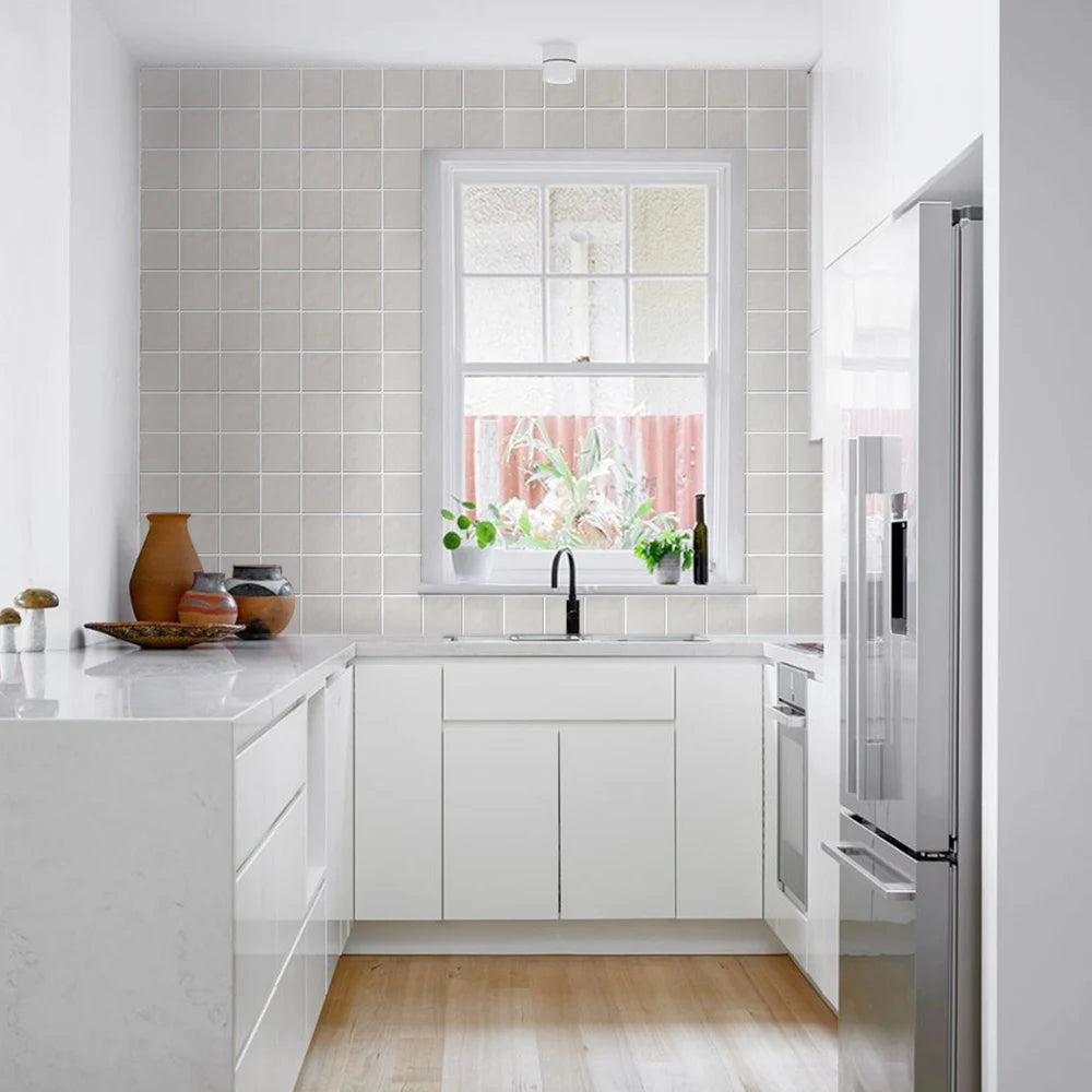 Modern kitchen with white cabinets, stainless steel refrigerator, and a window with plants.