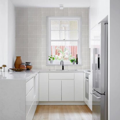 Modern kitchen with white cabinets, stainless steel refrigerator, and a window with plants.